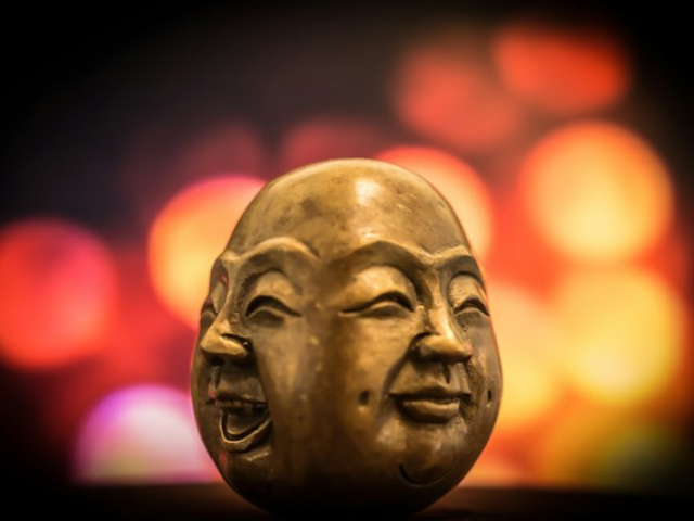 A golden buddha head with two faces, one laughing, one blank to. illustrate our rules around emotions