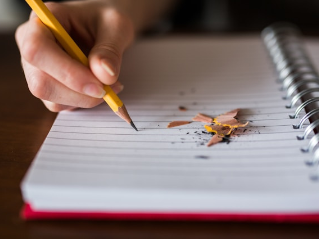 Photo of a pencil on a notebook with pencil shavings next to it to illustrate the power of writing prompts.