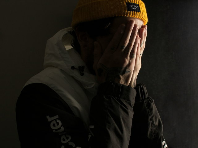Man in yellow hat covering his hands in shame.