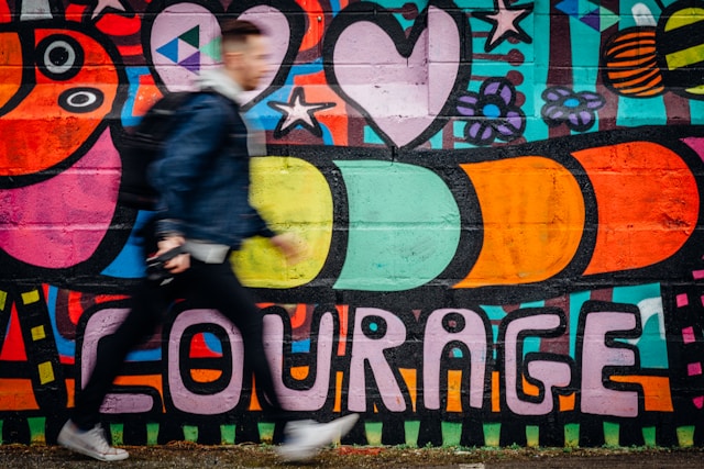 Photo of man walking past a wall with the word courage painted on it to illustrate brave spaces.
