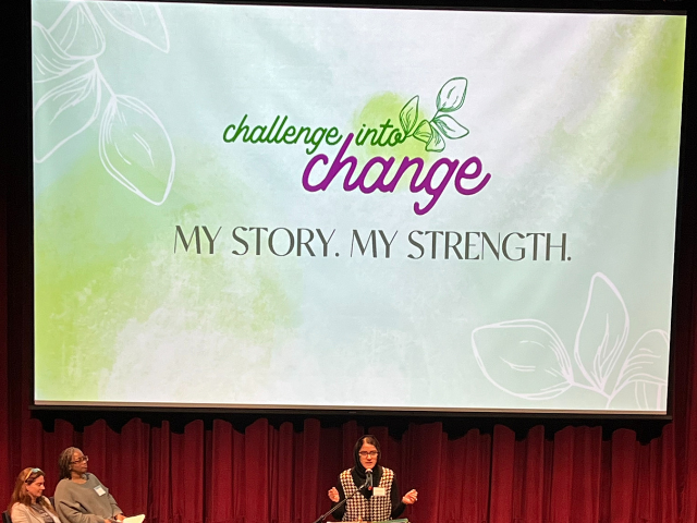 Photo for let community crack open of a backdrop that says challenge into change, my story, my strength above writer speaking at a podium