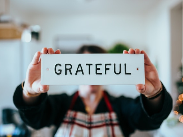 Photo with a person wearing a checked shirt and black sweater holding up a sign that says grateful to illustrate the importance of gratitude