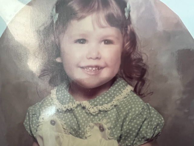 Photo of me at mine months old, a white baby with long brown curls wearing a blue gingham jumper to illustrate how my voice changed just like Peter Brady's did.