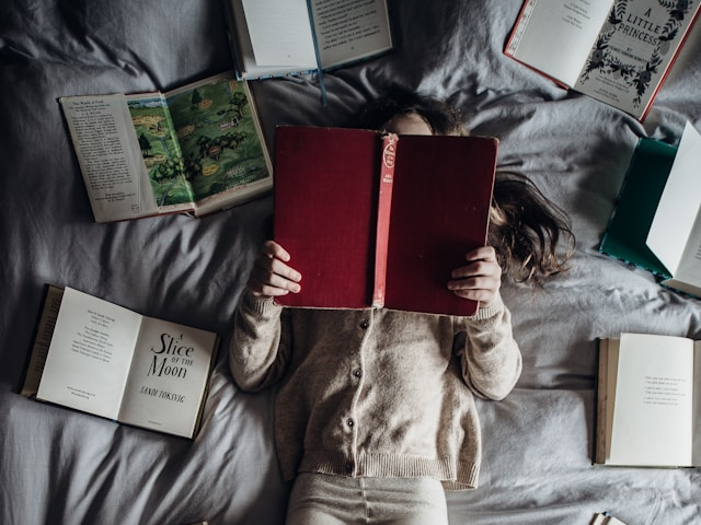 Photo of a woman laying down while reading a book and surrounded by books to illustrate reclaiming your power